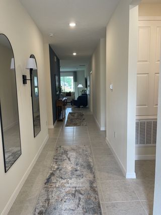 A modern hallway with sleek mirrors, elegant light fixtures, and a tiled floor leading to a cozy living space.
