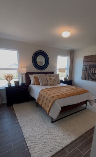 A stylish bedroom in The Granary home, featuring a plush bed with decorative pillows, a round mirror, dark wood furniture, and gray tile flooring (San Antonio, TX).