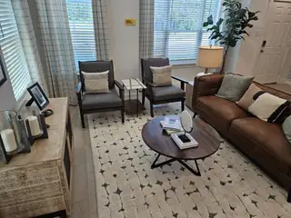Model Home A cozy living room featuring a plush brown sofa, patterned rug, and elegant decor with ample natural light from large windows.