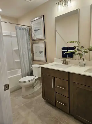 A contemporary bathroom featuring dual sinks, framed artwork, and sleek cabinetry, complemented by modern lighting.