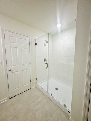 Model Home A sleek glass-enclosed shower with white tile, next to a white door in a modern bathroom.