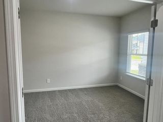 Model Home A bright, carpeted room with soft gray walls and large window flooding light, creating a cozy, inviting space.