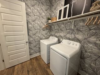 A chic laundry room with a nature-inspired wallpaper, wood floors, and white appliances for a clean, modern look.