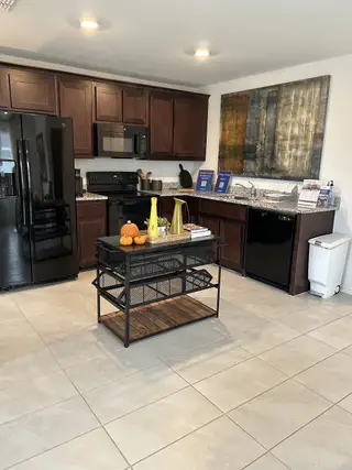 Model Home A cozy kitchen with dark cabinetry, black appliances, and a sleek granite countertop.