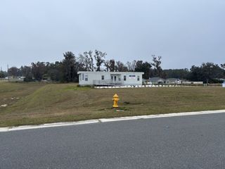 A modern sales office set in a grassy area with nearby homes in Bennah Oaks by Highland Homes of Florida (Belleview, FL).