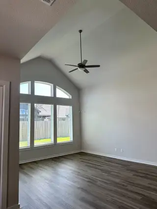 A spacious room with vaulted ceilings, hardwood flooring, large arched windows, and a ceiling fan.