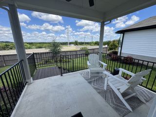 Model Home A cozy porch with white chairs, a patterned rug, and a lovely backyard view under a blue sky.