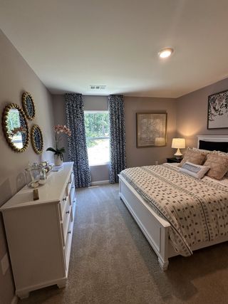 Model Home A cozy bedroom with a white dresser, patterned curtains, elegant mirrors, and plush bedding.