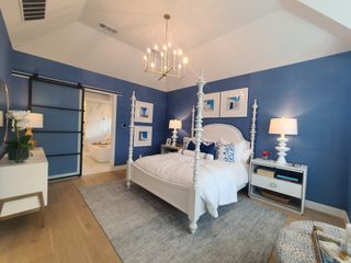 A chic bedroom with blue walls, white four-poster bed, elegant lighting, and a barn door leading to a stylish bathroom.