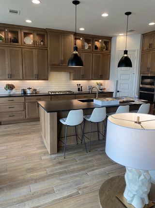 A modern kitchen featuring wood cabinetry, sleek black countertops, pendant lighting, and a central island with seating.