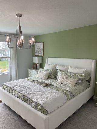 Model Home A serene bedroom with a plush bed, soft green accents, and elegant chandelier lighting.