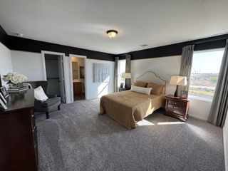 A spacious bedroom with cozy carpeting, elegant neutral decor, and ample natural light through large windows.