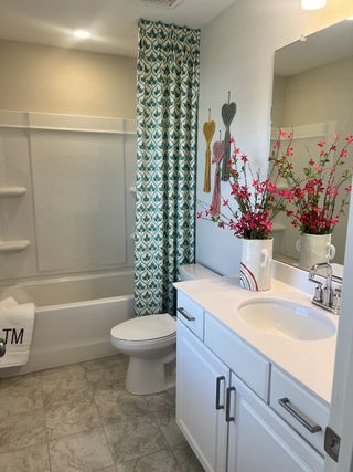 A bright bathroom with a white vanity, stylish hardware, and a patterned shower curtain, complemented by vibrant floral décor.