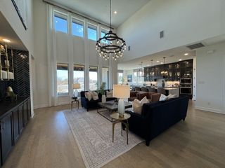 A spacious, elegant living area with high ceilings, a grand chandelier, dark cabinetry, and large windows flooding light inside.
