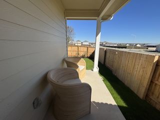 Model Home A cozy patio with modern wicker chairs, a wooden fence, and lush green grass under a clear blue sky. Perfect for relaxing outdoors.