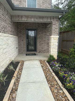 Street view Charming entrance with brick and stone accents, vibrant flowers in Lakes at Black Oak by Century Communities (Magnolia, TX).