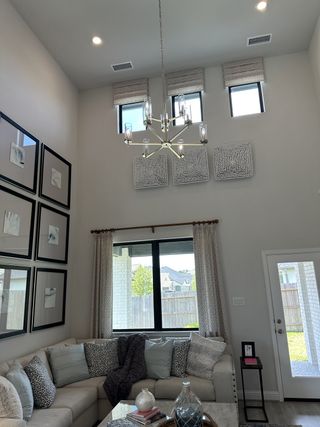 A stylish living room with high ceilings, modern chandelier, and cozy sectional sofa adorned with patterned cushions.