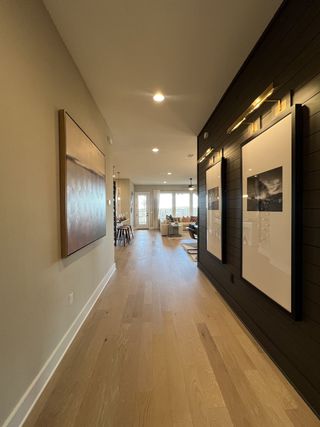 A modern hallway with wood floors, elegant artwork, and sleek lighting leading to a cozy living area.