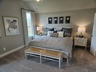 A cozy bedroom with elegant decor, featuring plush bedding, framed artwork, and soft carpeting for ultimate comfort.