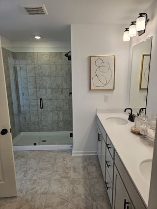Model Home Modern bathroom with a glass-enclosed shower, dual sinks, and elegant lighting, accented by contemporary wall art.