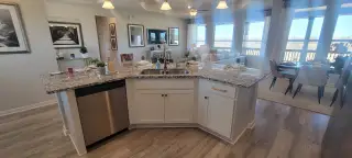 A modern kitchen with a granite island, stainless steel appliances, and an open living-dining area with large windows.