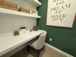 A cozy study nook with a sleek white desk, green accent wall, and motivational artwork, ideal for focused work or study.