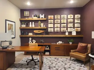 A sophisticated home office with rich wood furniture, decorative shelves, and geometric wall art.