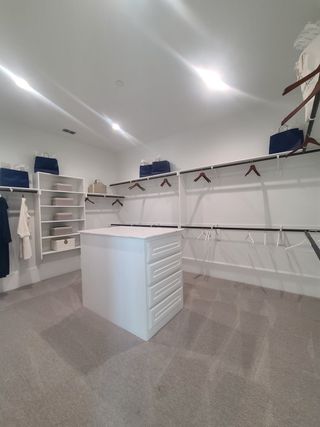 A spacious walk-in closet featuring white shelving, ample hanging space, and a central island with drawers.