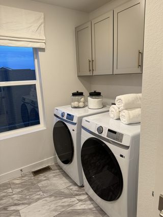 A modern laundry room with sleek appliances, ample cabinet storage, and chic marble-style flooring.