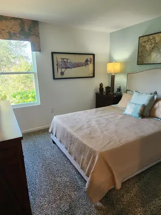 A cozy bedroom with soft carpeting, a decorative accent wall, and natural light in Copes Landing by D.R. Horton (Jacksonville, FL).