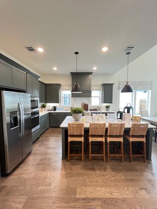 A modern kitchen with dark cabinets, sleek stainless appliances, a spacious island, and warm wood flooring.