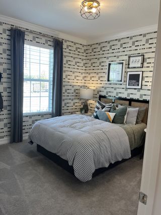 A cozy bedroom with patterned wallpaper, striped bedding, stylish wall art, and soft carpet.