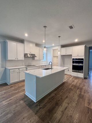 A modern kitchen with white cabinetry, a marble island, pendant lighting, and wood flooring.