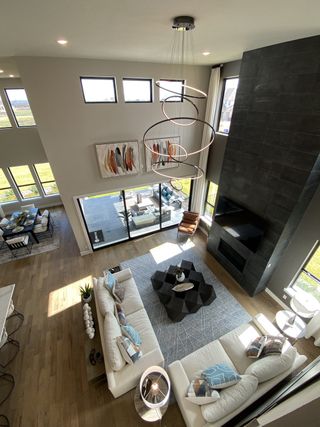 A modern living room with tall ceilings, sleek chandelier, and expansive windows, featuring cozy seating and elegant decor.