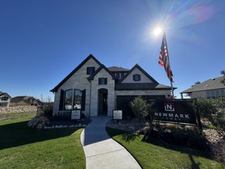 Street view A striking stone-clad home with elegant black shutters and lush landscaping in La Cima by Newmark Homes (San Marcos, TX).
