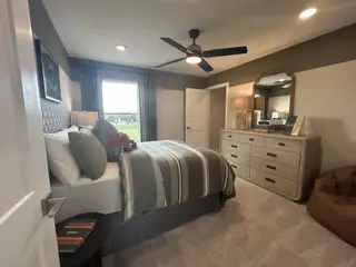 A cozy bedroom featuring a modern ceiling fan, plush bedding, and a stylish dresser with elegant decor.