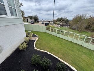 A lush backyard with manicured lawn and stone-bordered garden in Whisper Valley by GFO Home (Manor, TX).