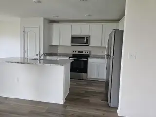 A modern kitchen with granite countertops, stainless steel appliances, white cabinets, and wood-style flooring.