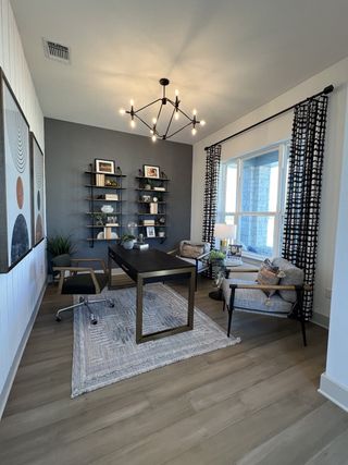 A sleek home office with a dark accent wall, open shelving, and a chic chandelier, creating a stylish and productive workspace.