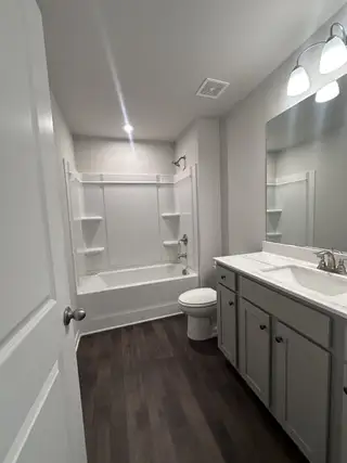 A modern bathroom with a sleek bathtub, elegant vanity, and tasteful lighting on dark wood flooring.