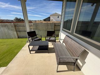 A cozy patio with modern wicker seating, a small table, and a view of a fenced backyard.