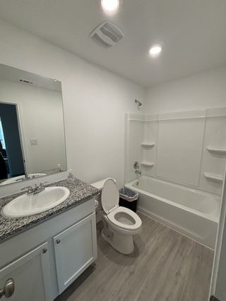 Model Home A clean bathroom with a granite countertop, white cabinets, a tub/shower combo, and gray wood-look flooring.