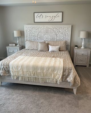 A cozy bedroom with an ornate headboard, plush bedding, soft lighting, and neutral tones for a serene atmosphere.