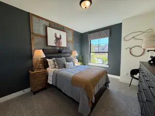 A cozy bedroom with dark accent walls, rustic wood elements, and a large window overlooking the outdoors.