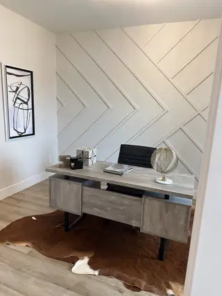 A modern office with a sleek desk, abstract art, and stylish accent wall, complemented by a cowhide rug.
