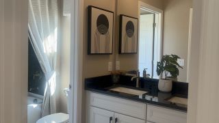A modern bathroom with dual sinks, black countertops, abstract art, and natural light streaming through a window.