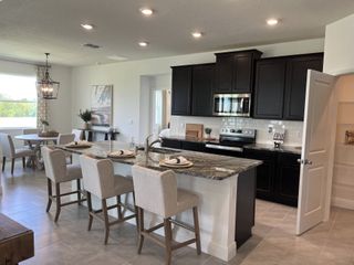 Model Home Modern kitchen with dark cabinets, granite island, and elegant dining area. Bright and inviting space with stylish lighting.