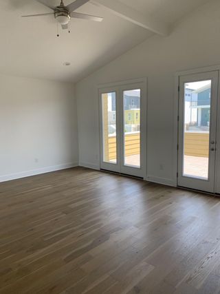 An airy room with hardwood floors, vaulted ceiling, and large windows offering plenty of natural light.