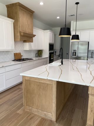 A modern kitchen with wood accents features white cabinetry, marble countertops, and sleek black pendant lighting.