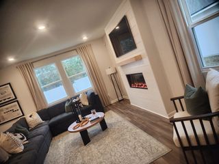 A cozy living room features a sectional sofa, modern fireplace, large windows, and soft lighting, creating an inviting atmosphere.